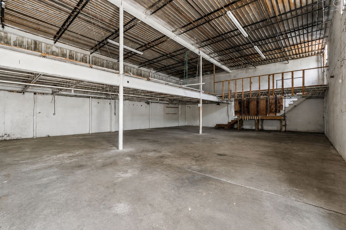 Current condition: empty hall with bare slab, exposed deck, partial wood-framed mezzanine and temporary stairs